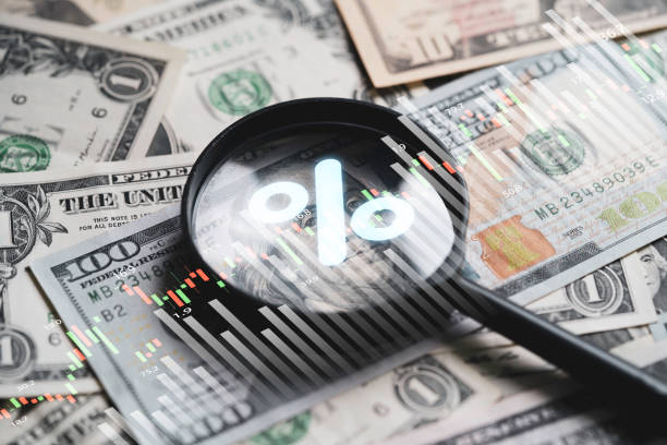 Image of a magnifying glass focusing on a percentage symbol, set against a background of money, representing the impact of interest rates on home buying trends and dreams.