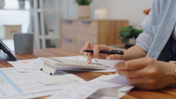 A hand with a pen calculating figures on a calculator at a work desk, representing the financial strategies homeowners and buyers should implement before 2025.